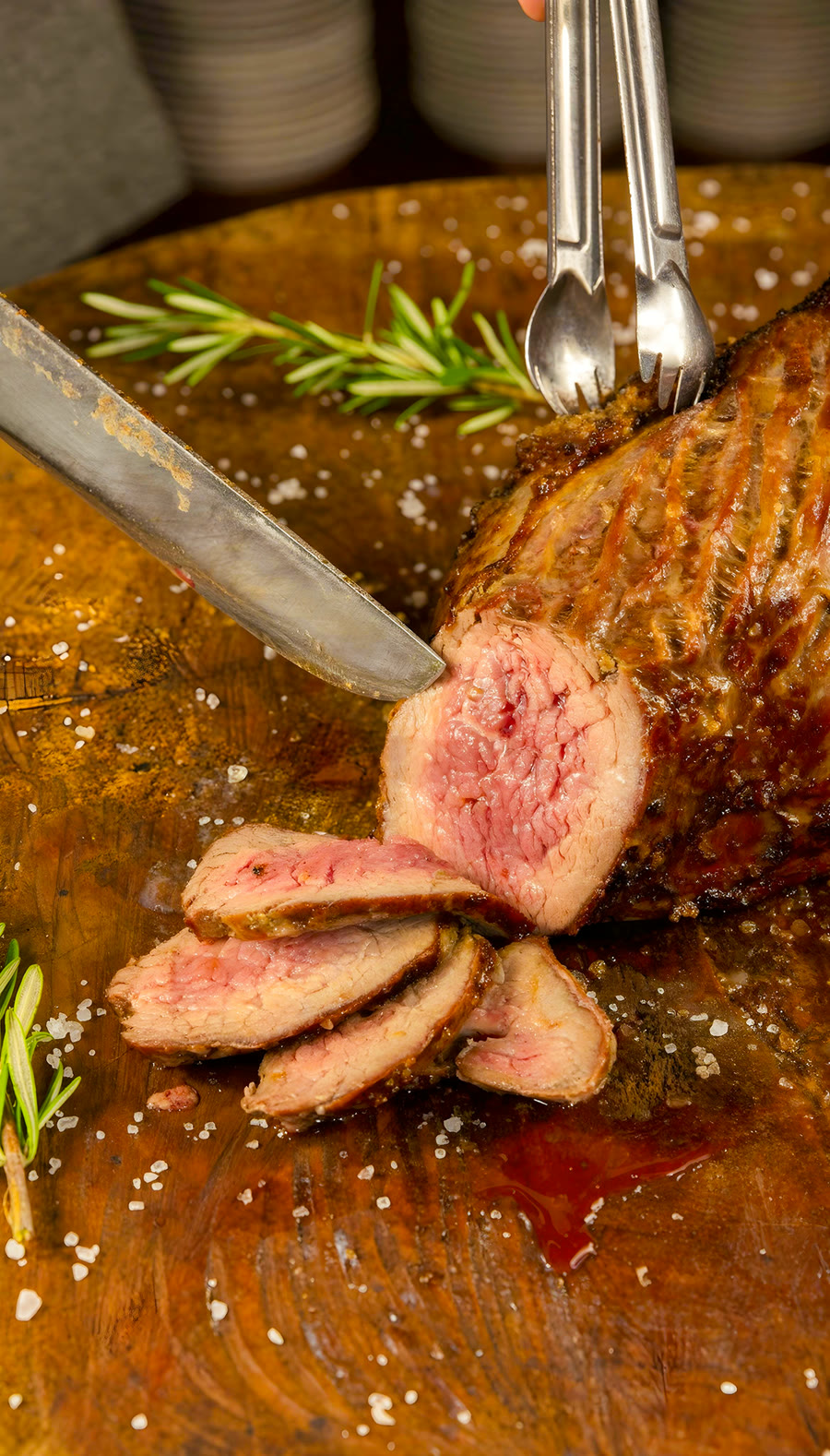 Corte de carne nobre sendo fatiado sobre tábua de madeira com alecrim
